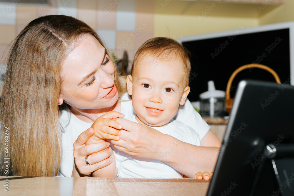 Motherhood, parenting, childcare. Happy family together, mom playing with smiling baby while sitting with tablet in kitchen at table. Young mother hugging cheerful child, little son looking at camera Motherhood, parenting, childcare. Happy family together, mom playing with smiling baby while sitting with tablet in kitchen at table. Young mother hugging cheerful child, little son looking at camera