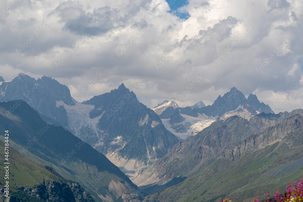 A panoramic view on high Caucasus mountains in Georgia. There are high, snowcapped peaks in the back. Thick clouds above the peaks. Idyllic landscape. Calmness and meditation. Natural remedy