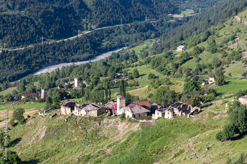 A panoramic view on Zhabeshi, a mountain village in Georgia. A few lookout towers popping up. There is a river in the back. Lush green slopes. photo