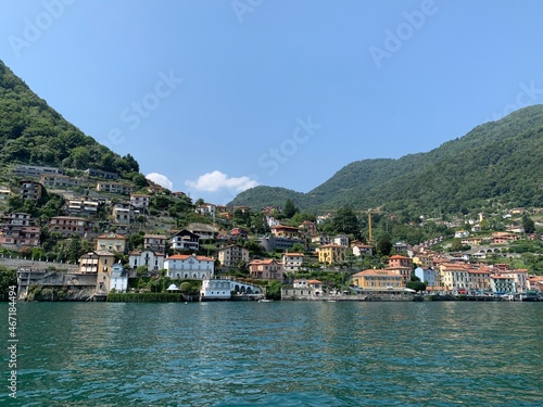 Skyline of Argegno town with houses on hills and mountains. Landscape of Como Lake (Lago di Como) shore. View from the boat. It is a famous Italian vacation place. Argegno, Como Lake, Lombardy, Italy.