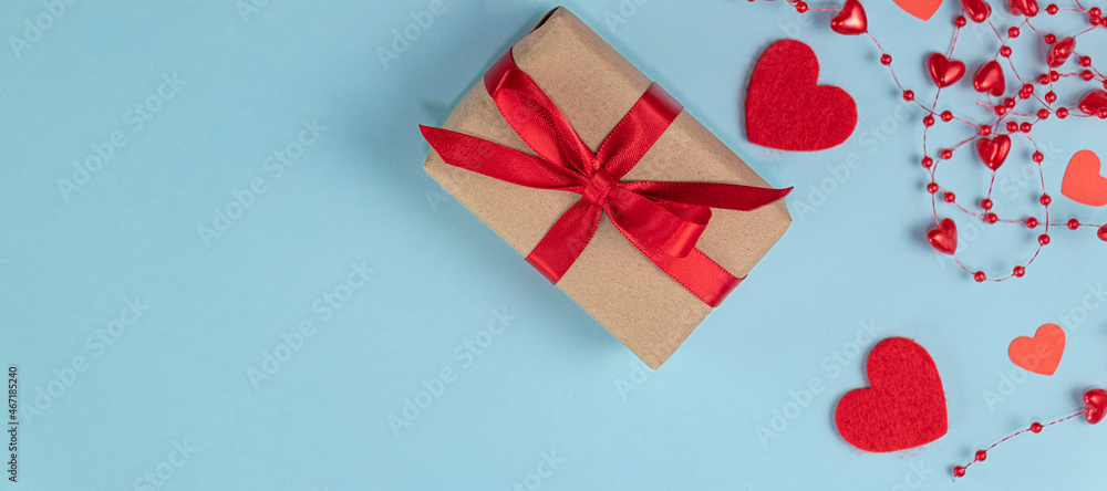 banner with flat lay gift with a red ribbon on a pastel blue background with red beads with hearts. banner with flat lay gift with a red ribbon on a pastel blue background with red beads with hearts.