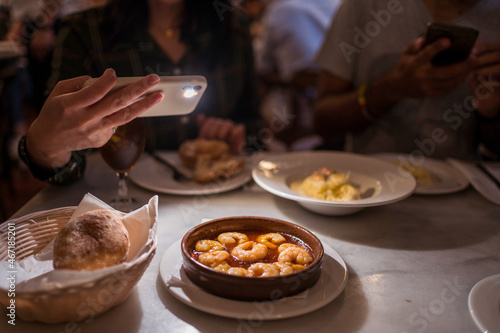 Unrecognizable woman photographing bowl of delicious gambas al ajillo in restaurant photo
