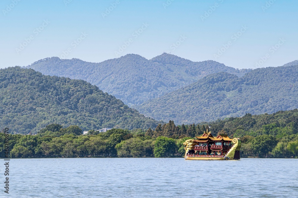 A Dragon Tour Boat crossing green hills and mountains of the West Lake, Hangzhou, China