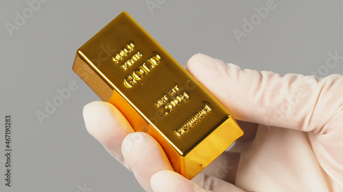 Gold bar in hand and wear latex glove isolated on grey background. photo