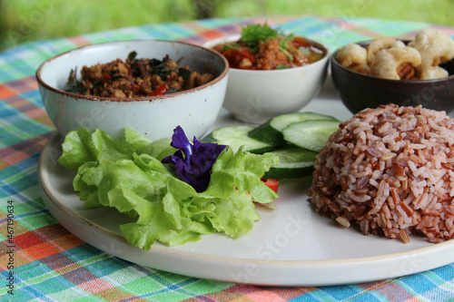 Thai style food, rice with stir fried basil with pork, chili paste, pork kappa and vegetable on white plate.