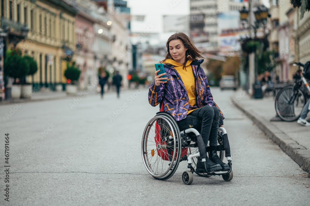Obraz premium Woman in wheelchair using a smartphone while out in the city
