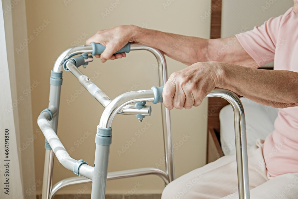 Cropped shot of an elderly woman in nursing home room holding walking frame with wrinkled hand. Senior lady grabbing metal walker's handles. Interior background, copy space, close up. Cropped shot of an elderly woman in nursing home room holding walking frame with wrinkled hand. Senior lady grabbing metal walker's handles. Interior background, copy space, close up.