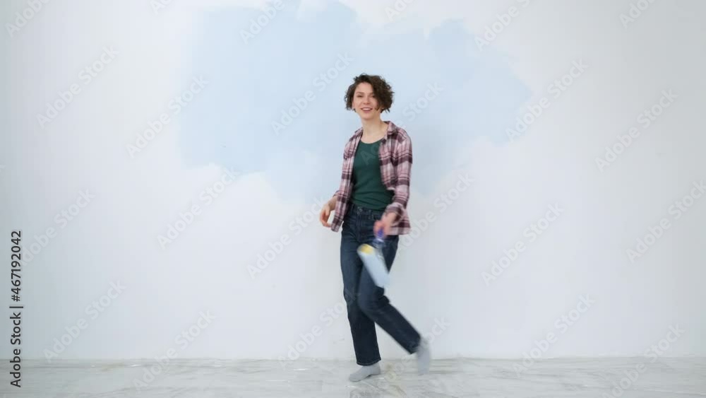A young adult cheerful woman with blue paint using a roller. Repair and renovation of the design of home room apartment. DIY repair of the house. A young adult cheerful woman with blue paint using a roller. Repair and renovation of the design of home room apartment. DIY repair of the house.
