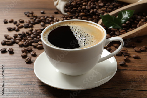 Cup of aromatic hot coffee and beans on wooden table, closeup