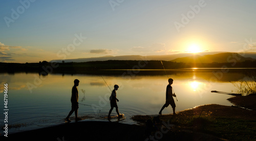 Silhouettes of fishing boys are walking home after fishing the lake in the evening sun, Reservoir Amphoe Wang Saphung Loei Thailand
