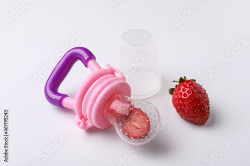 Nibbler with fresh strawberries on white background. Baby feeder