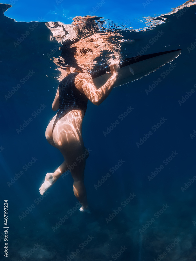 Sexy surfer girl swimming with board in blue sea. Underwater view with woman and surfboard
