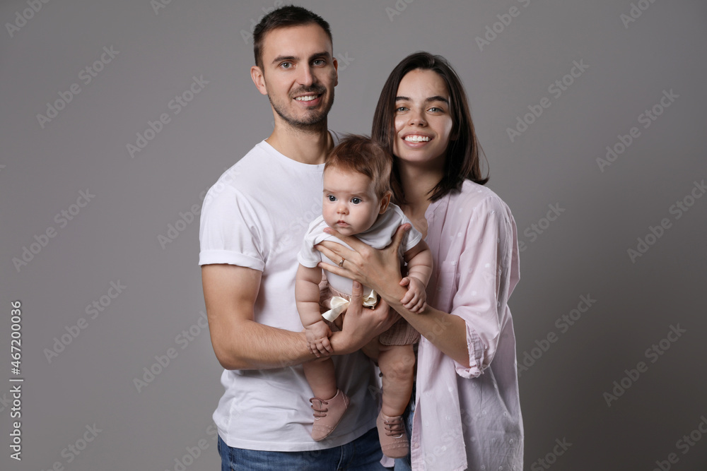 Happy family. Couple with their cute baby on grey background Happy family. Couple with their cute baby on grey background
