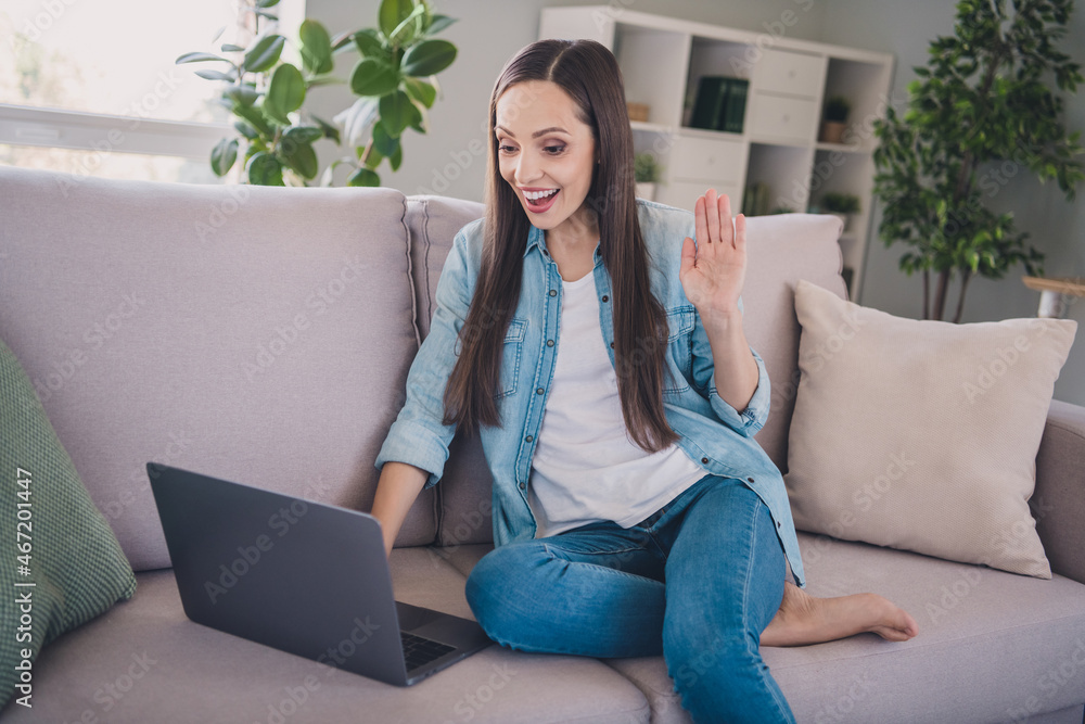 Portrait of attractive cheerful long-haired woman sitting on divan using laptop calling waving hi hello at home indoors