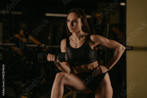 A sporty woman is doing dumbbell curls with her elbow on a knee © Roman Tyukin