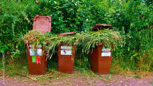 Prague, Czech Republic - June 15, 2021: Three trash cans for biowaste full of grass from nearby public garden area. The bins are so full they can't be fully closed. photo