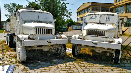 Two white trucks Praga V3S standing inside renovated brownfield area called Pragovka. There are some industrial buildings in the background. photo