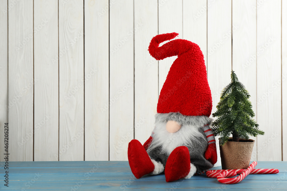 Fototapeta premium Cute Christmas gnome, small decorative fir tree and candy canes on turquoise table against white wooden background. Space for text