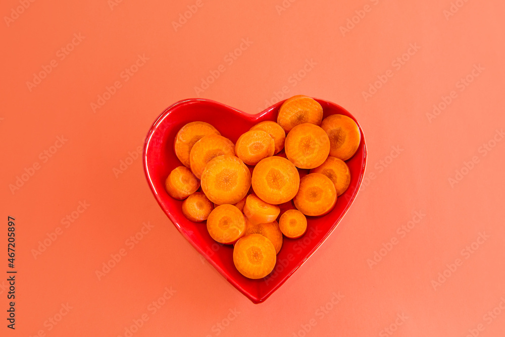 Sliced carrots in heart-shaped pot on orange background. Sliced carrots in heart-shaped pot on orange background.