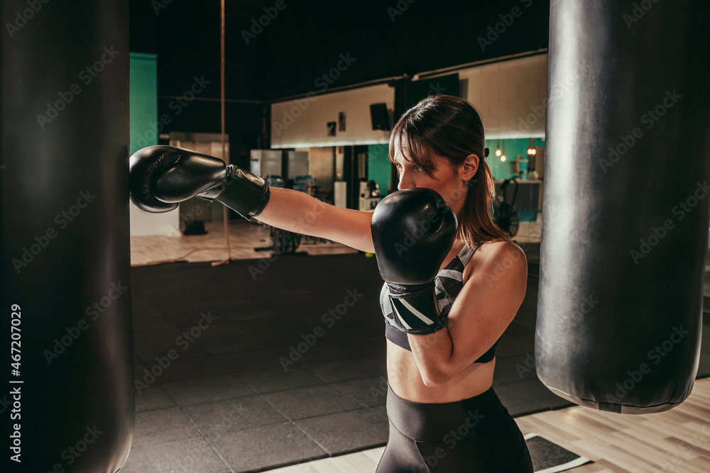 Woman training boxing at gym. Strong athletic young brunette woman training self-defense punches in boxing gloves. Concept female sport.