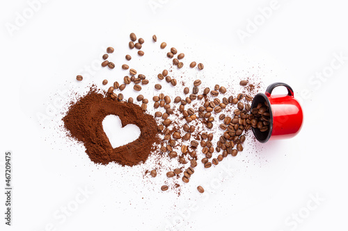 caneca vermelha de ferro derramando grãos de café e pó de café com um formato de coração em seu centro em fundo branco photo