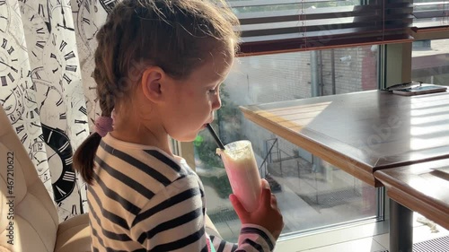 Happy kid drinking strawberry milkshake in cafe. 5 years old girl. Beautiful sun glare.