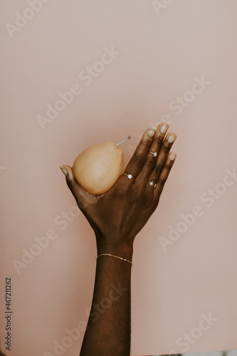 Black hand holding a pear wearing a gold bracelet photo