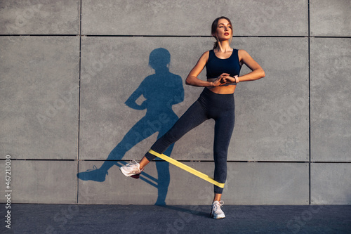 sporty woman doing exercises with resistance band, fitness woman doing leg exercises with yellow fitness rubber band photo