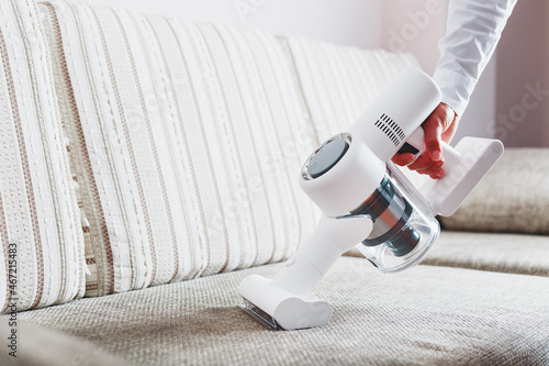 Fotografía A man's hand holds a modern wireless vacuum cleaner for cleaning the sofa in the house