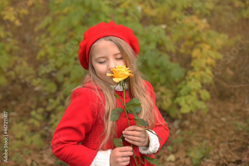 a beautiful blonde girl in a red coat and beret holds a yellow rose garden in autumn