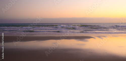 Ocean waves crashing on sand shore under pinkish sky photo