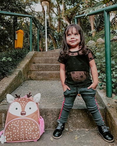 Smiling toddler girl standing on stairs beside deer-themed backpack photo