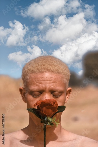 Topless man with albinism holding red rose in desert photo