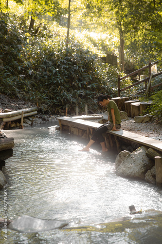 Woman in brown shirt sitting on brown wooden bridge over river