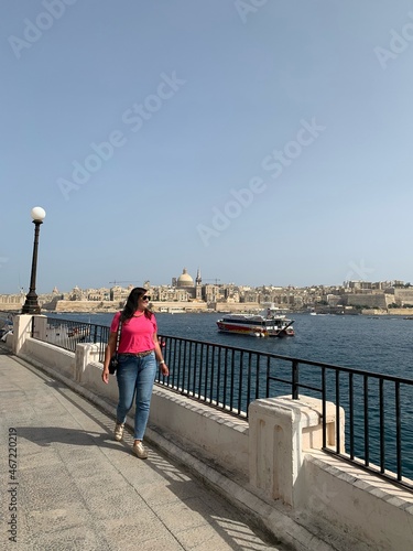Woman in pink with sunglasses walking by waterside photo