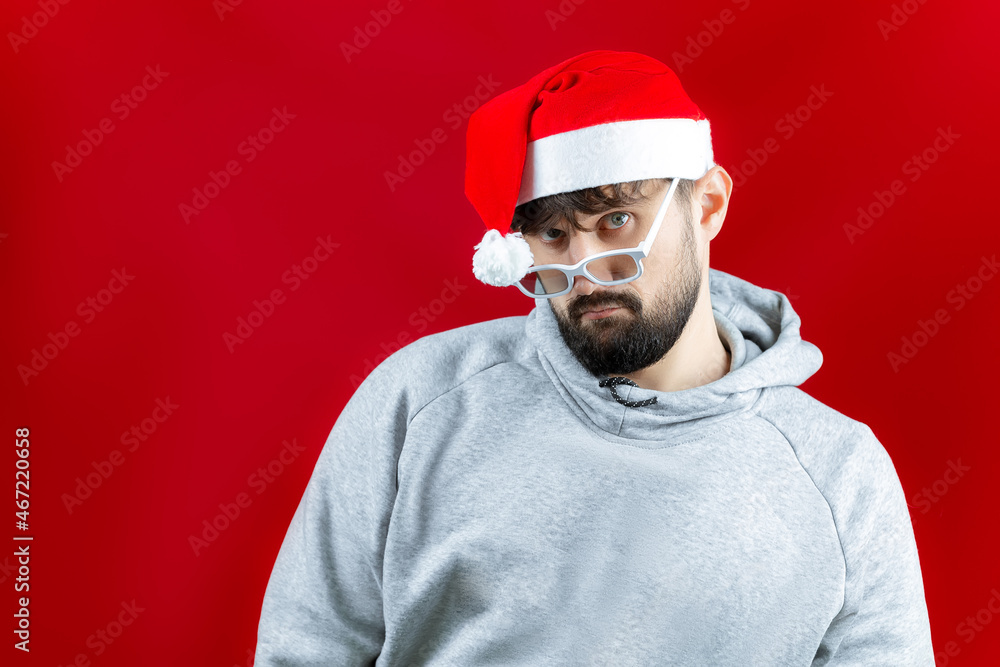 a man in a red Santa Claus hat lowered his glasses on the bridge of his nose and looks surprised a man in a red Santa Claus hat lowered his glasses on the bridge of his nose and looks surprised