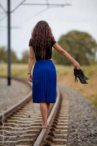 Woman walking on the train railings barefoot holding her heels photo