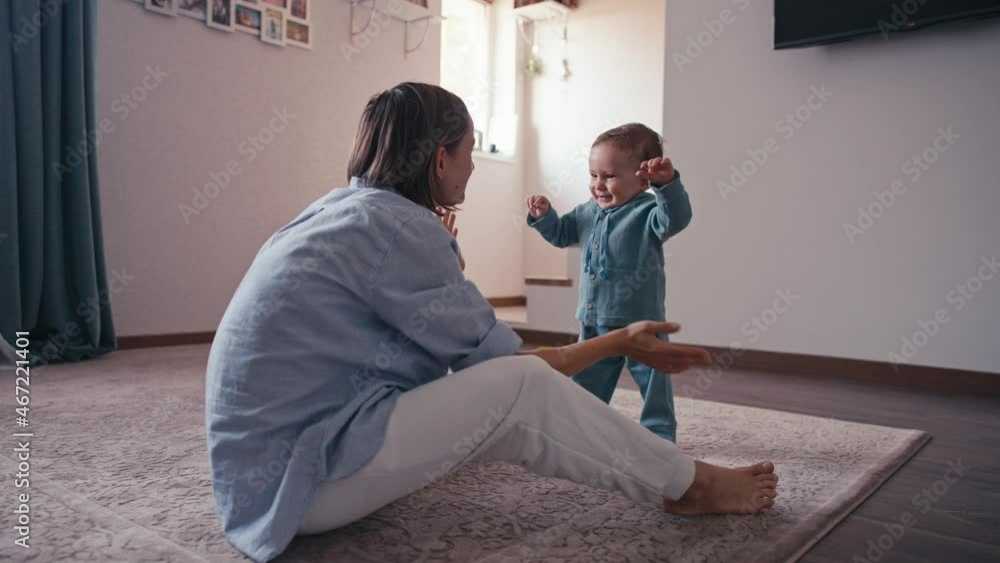 Lovely caucasian baby biy learning to walk taking first step walk to his mother at home. Baby boy walking on the floor with bare foot. Cute baby boy learning to walk. First steps baby. Lovely caucasian baby biy learning to walk taking first step walk to his mother at home. Baby boy walking on the floor with bare foot. Cute baby boy learning to walk. First steps baby.