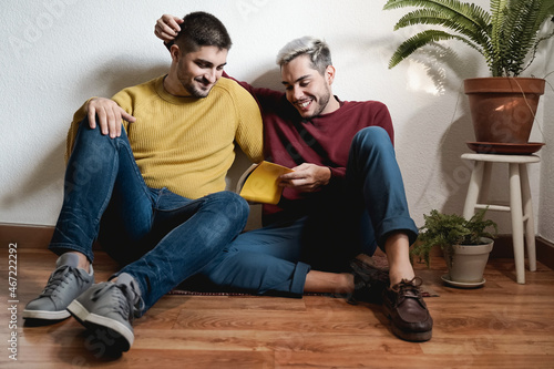 Gay male couple reading book together indoor at home - LGBT homosexual love moments concept