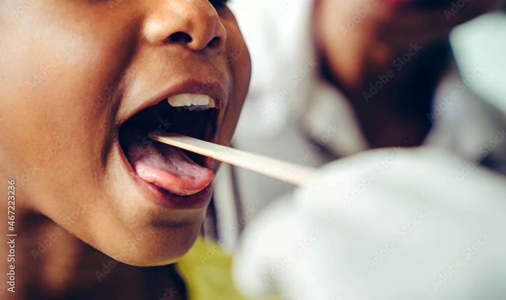 Pediatrician examining little girl's throat with tongue depressor