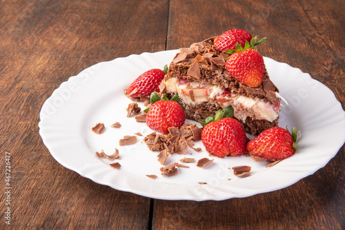 Chocolate cake, a tasty slice of chocolate cake with strawberries on a white plate on rustic wood, abstract background, selective focus.