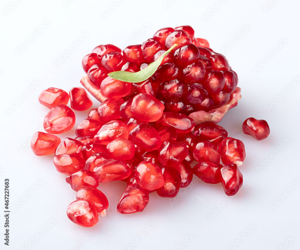 A piece of a young pomegranate with a textured peel and a mountain of beautiful young pomegranate seeds with an elegant fresh pomegranate leaf isolated on a white background with a shadow. Close-up A piece of a young pomegranate with a textured peel and a mountain of beautiful young pomegranate seeds with an elegant fresh pomegranate leaf isolated on a white background with a shadow. Close-up