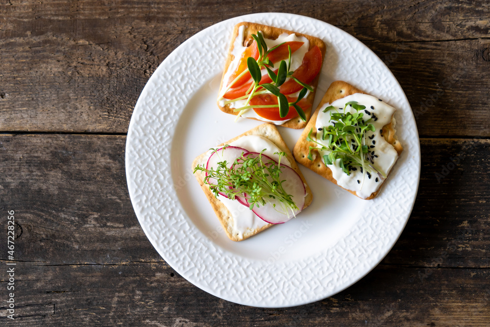 Set of Bruschett with cream cheese and tomato spread. Radish, micro green and flaxseed in food. Simple food on the plate. Breakfast in a white plate top view. Wooden background. Cracker Set of Bruschett with cream cheese and tomato spread. Radish, micro green and flaxseed in food. Simple food on the plate. Breakfast in a white plate top view. Wooden background. Cracker
