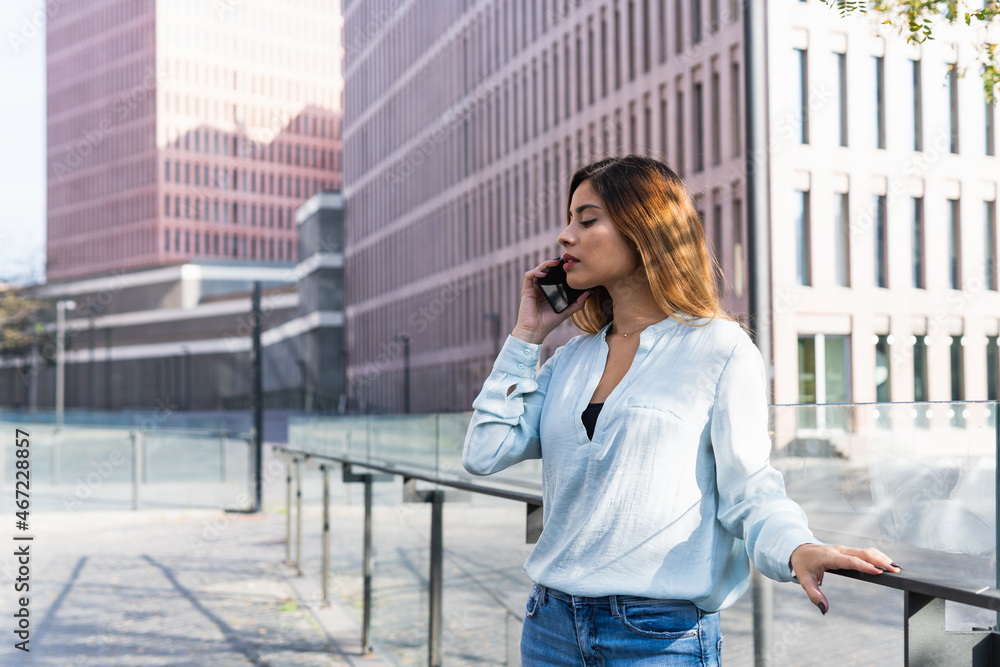 Fototapeta premium Attractive young businesswoman talking on smartphone with business partners outdoors, professional female architect working on new project surrounded by buildings