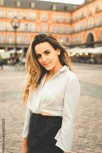 Young caucasian woman portrait with a white blouse and a black skirt at Madrid's Plaza Mayor, Spain.