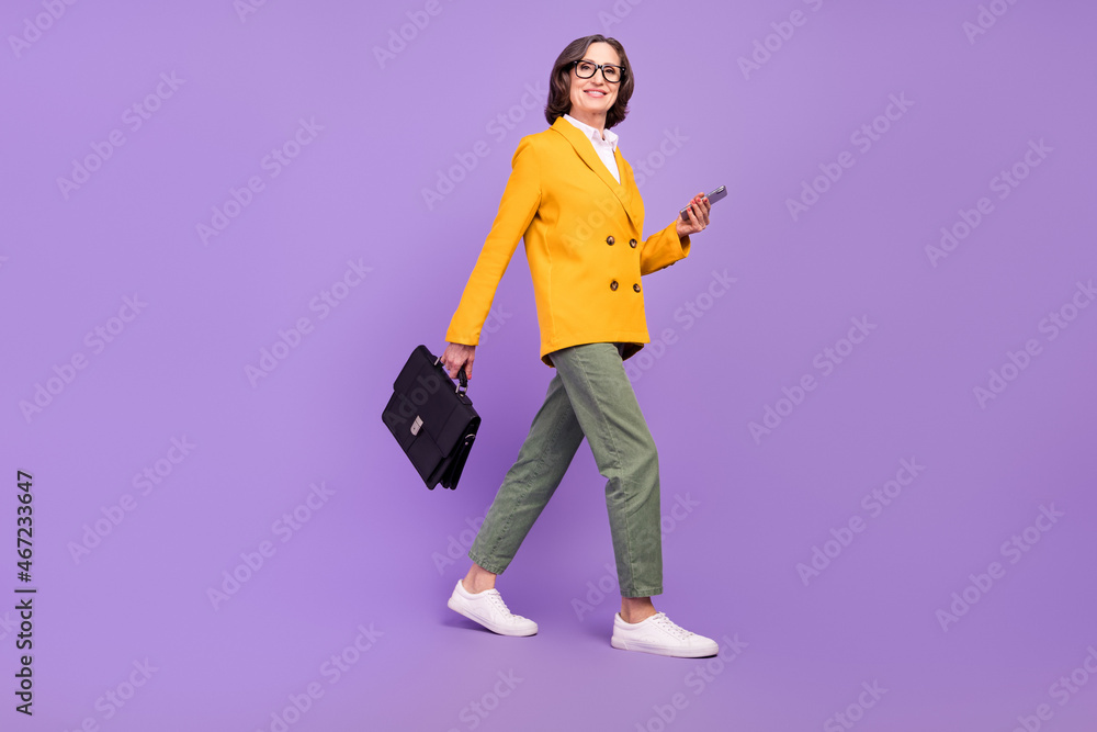 Full length photo of positive happy old lady hold suitcase phone business meeting walk isolated on purple color background Full length photo of positive happy old lady hold suitcase phone business meeting walk isolated on purple color background