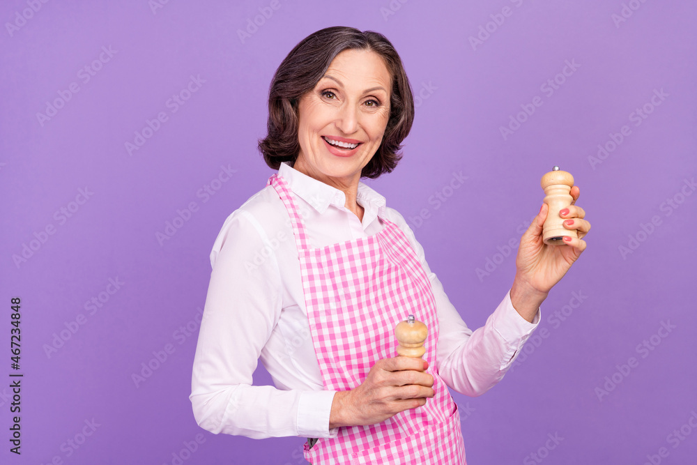 Photo of positive happy retired old woman hold salt pepper cook meal dinner isolated on purple color background Photo of positive happy retired old woman hold salt pepper cook meal dinner isolated on purple color background