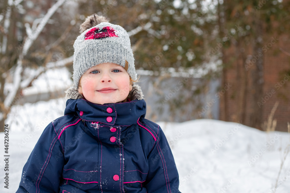 Small happy smiling child portrait outdoors in winter. Little girl in hat and jacket playing outside with snow in cold weather.