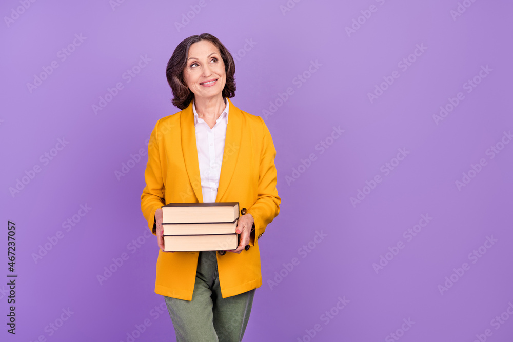 Photo of optimistic professor grey aged lady hold books look empty space wear yellow jacket isolated on purple color background Photo of optimistic professor grey aged lady hold books look empty space wear yellow jacket isolated on purple color background