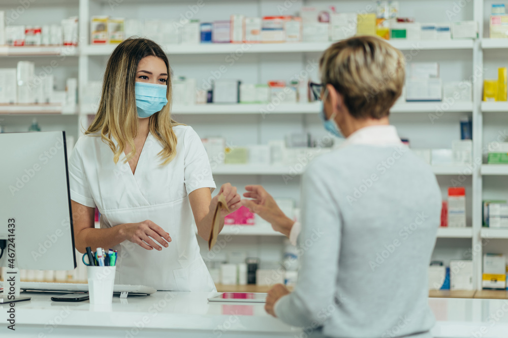 Pharmacist wearing protective mask and serving a customer patient in a pharmacy Pharmacist wearing protective mask and serving a customer patient in a pharmacy